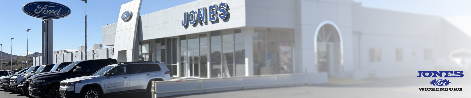 Exterior view of a Ford dealership building and vehicle lot featuring trucks and SUVs.