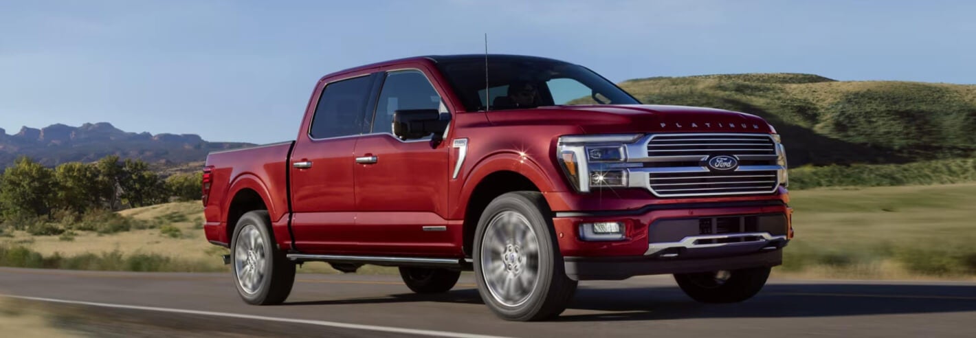 A red Ford F-150 drives down a remote highway at golden hour.